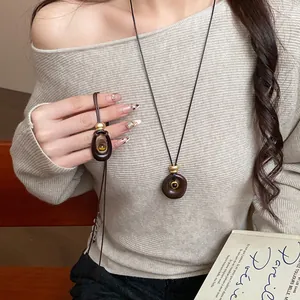 Détail d'un collier pendentif ovale en résine avec pierre œil de tigre sur un modèle.