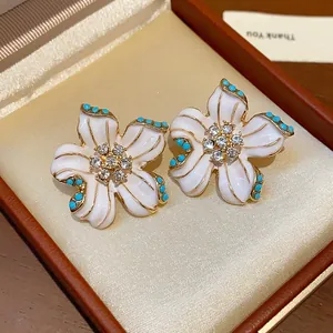 Close-up of vintage flower stud earrings with white enamel and sparkling rhinestones