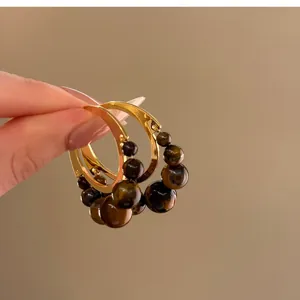 Dettaglio di orecchini a cerchio vintage stile Maillard con perline di occhio di tigre