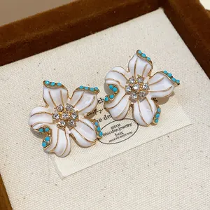 Close-up of vintage flower earrings with white enamel petals and turquoise accents