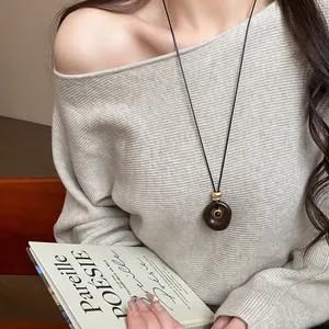 Gros plan d'un pendentif ovale en résine brune avec pierre œil de tigre sur un pull gris