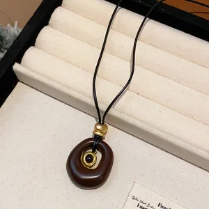 Gros plan d'un collier pendentif ovale en résine exposé sur un plateau à bijoux crème.