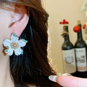 Close-up of vintage flower stud earring with white enamel and rhinestone center on ear