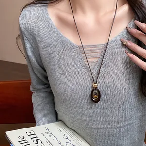 Détail d'un collier pendentif ovale en résine avec œil de tigre porté par un mannequin.