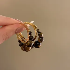 Primo piano di orecchini a cerchio dorati con perle di occhio di tigre