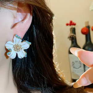 Elegant white flower earring with crystals and blue accents on model's ear