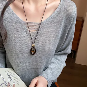 Détail d'un long collier ovale en résine avec pierre œil de tigre sur un pull gris