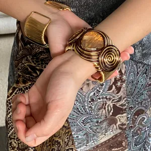 Macro detail of a twisted woven gold cuff with a large amber geometric glass stone.