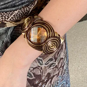 Detail view of a twisted wire-wrapped cuff bracelet with amber faceted glass gem.