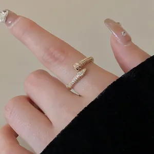 Detail view of a gold-toned snake-shaped open ring with sparkling cubic zirconia on a finger.