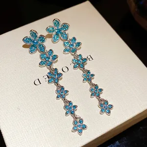 Close-up detail of silver needle dangle earrings with shimmering blue zircon flowers.