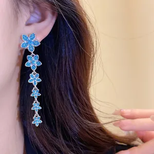 Close-up view of elegant blue zircon flower tassel earrings on model, silver jewelry.