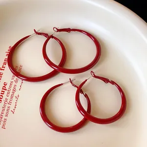 Close-up detail of glossy red paint hoop earrings on a decorative ceramic plate