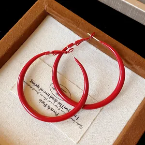 Detail shot of vintage red spray-painted hoop earrings on textured fabric background.