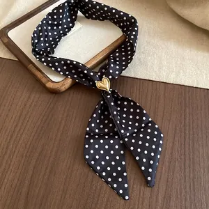 Primo piano della collana a sciarpa in seta a pois neri con ciondolo a cuore dorato.