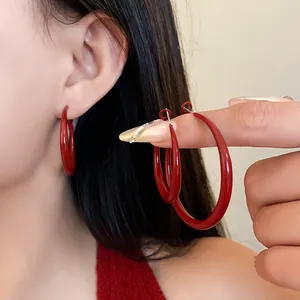 Macro view of minimalist vintage red spray-paint hoop earrings worn on ear and hand