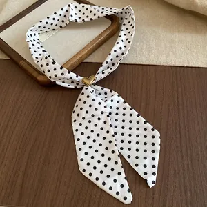 Dettaglio di una collana a sciarpa vintage bianca a pois neri con fibbia a cuore dorata