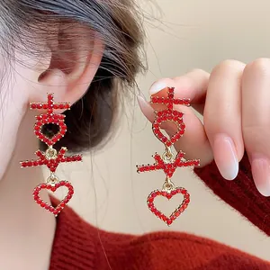 Detail view of gold earrings with red rhinestones and heart drop for Chinese New Year.