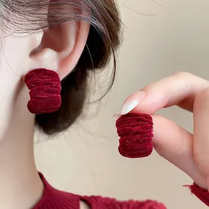 Close-up of red velvet pleated earrings showing textured detail and elegant wearing effect.
