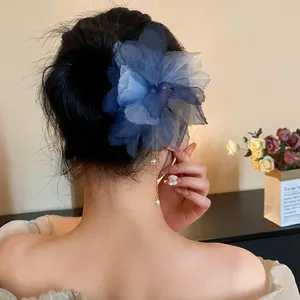 Back view of a blue chiffon flower hair pin with pearl tassels in a low bun hairstyle.