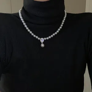 Detail shot of an elegant pearl necklace with a zircon waterdrop pendant on a black sweater.