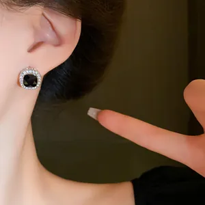 Elegant black square stud earring with a shimmering crystal halo shown on a model's ear.