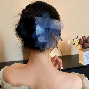 Detailed view of a blue chiffon flower hair pin with a delicate pearl tassel on a bun.