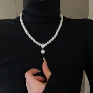 Detail of a pearl necklace with teardrop zircon pendant on a black sweater.