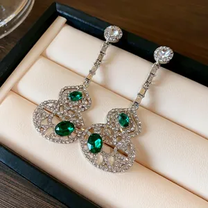Detailed macro shot of long hollow gourd earrings featuring emerald stones and sparkling crystals