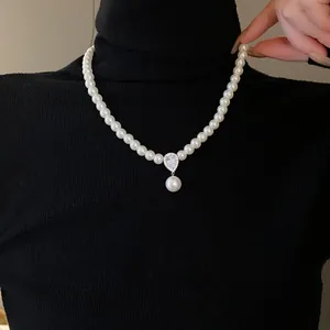 Close-up of elegant pearl necklace with zircon water drop pendant worn over black sweater