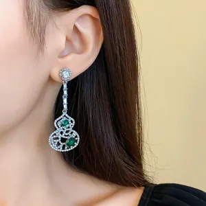 Close-up of elegant hollowed-out gourd drop earrings with silver needle and green gems