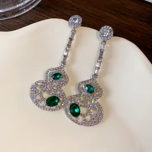 Detail view of silver-plated hollow gourd dangle earrings with green emerald-colored stones.