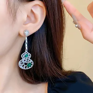 Close-up detail of elegant hollow gourd dangle earrings with green stones on silver needle.