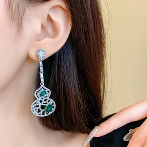 Detail view of long drop gourd-shaped earrings with emerald green stones and pave diamonds