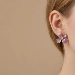 Close-up of elegant purple enamel flower earrings with pearl center on an Asian model