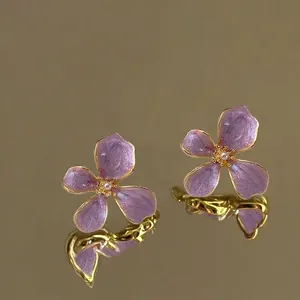 Detailed view of purple enamel flower earrings with pearl centers on gold trim