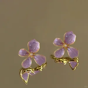 Close-up of purple flower earrings with pearl center and golden oil-drop texture.