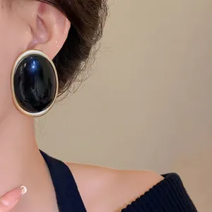 Elegant vintage oval black resin stud earrings with gold metal frame worn by model