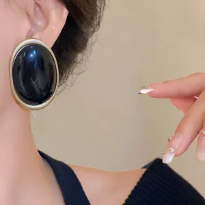 Detailed close-up of retro black oval resin earring with gold border worn by an Asian model