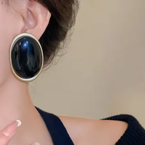Close-up of vintage black oval resin earring with a textured gold border finish.