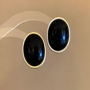 Detail of elegant oval black resin earrings with a minimalist silver-colored metallic border.