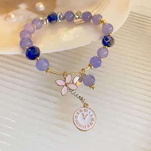 Detail view of purple glazed bead bracelet featuring a delicate clock and flower charms