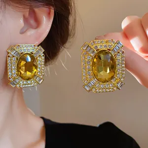 Detailed close-up of ornate gold square earrings with yellow gemstone and sparkling crystals