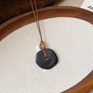 Dettaglio macro di un ciondolo etnico in resina nera su un vassoio di legno rustico