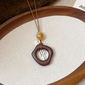 Dettaglio di una collana in resina stile etnico retrò con un ciondolo marrone unico.