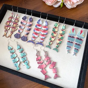 Collezione di orecchini etnici in legno a forma di pesce con vari motivi su vassoio.