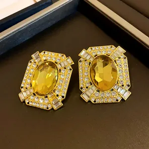 Detailed view of vintage gold earrings with large yellow oval gemstone and clear rhinestones.