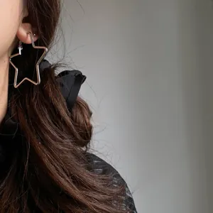 Close-up detail of a minimalist silver star-shaped hoop earring on a model's ear