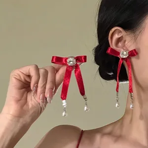 Primo piano di orecchini a fiocco rosso con strass eleganti e pendenti di perle bianche.