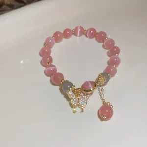 Detail of a pink cat-eye bead bracelet with a sparkling gold butterfly charm.